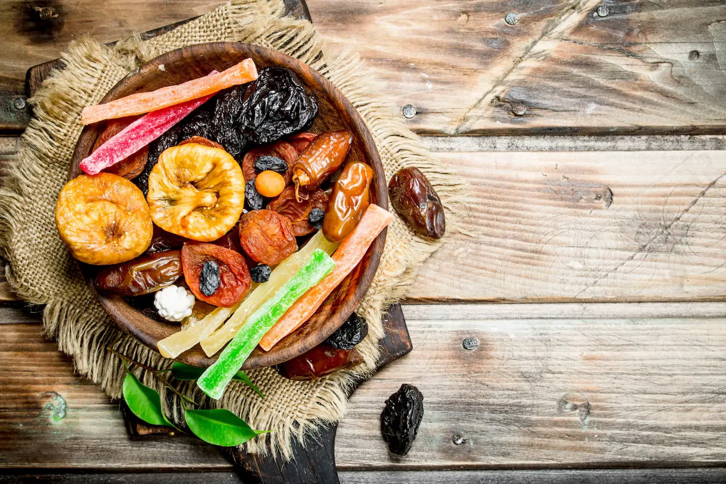 An image of various dried fruits in a bowl on a wooden table.